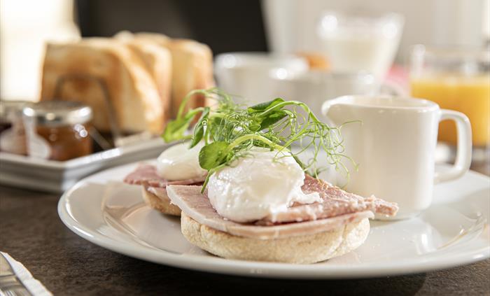 A plated eggs Benedict breakfast. 2 perfectly poached eggs, sat on top of freshly sliced ham on toasted muffin halves. Served with a hollandaise sauce